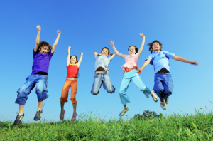 Group of five happy children jumping outdoors.